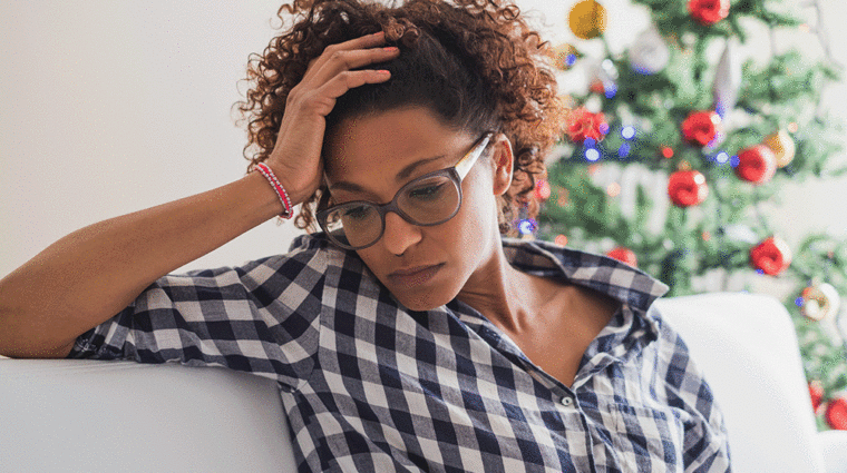 stressed woman sitting on couch in front of Christmas Tree