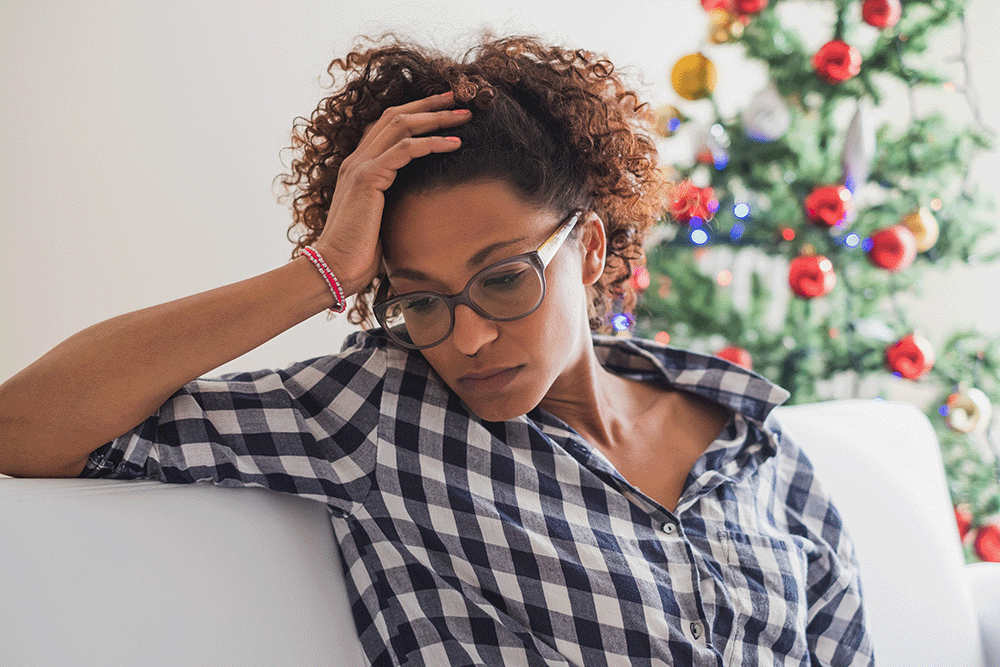 stressed woman sitting on couch in front of Christmas Tree