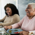 Happy black mother and daughter having fun eating healthy lunch at home
