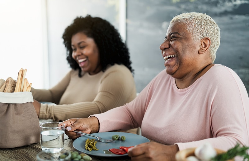 Happy black mother and daughter having fun eating healthy lunch at home