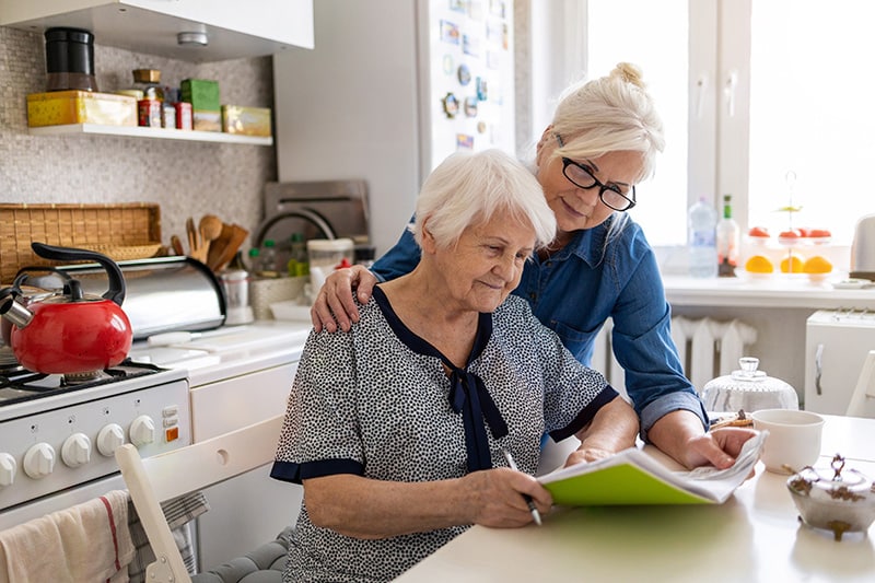 Older woman living at home and her caregiver at home in kitchen