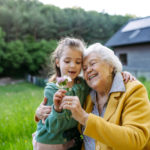 Granddaughter spending time with elderly grandma, picking wildlflowers, Senior lady in wheelchair spending time in nature