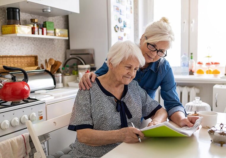 Older woman living at home and her caregiver at home in kitchen