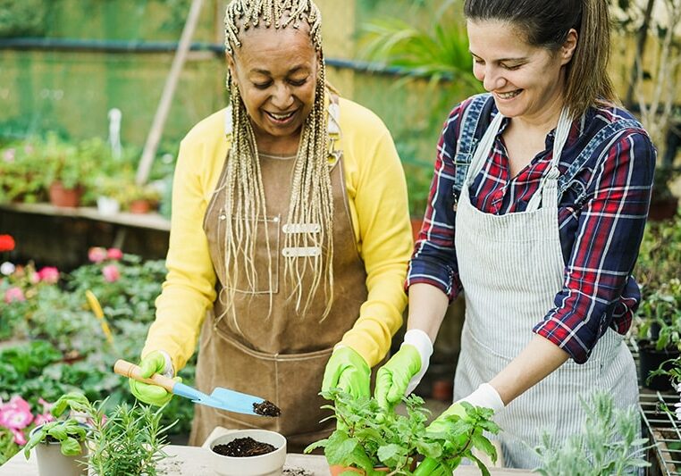 Two women gardening and smiling in greenhouse