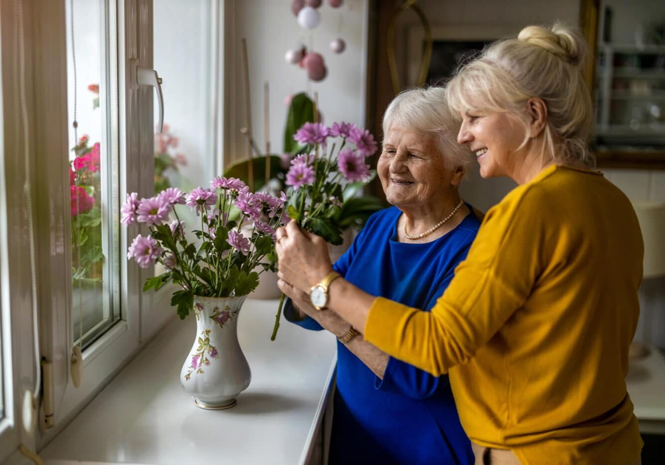 Daughter caregiver and older mother putting purple flowers in a vase