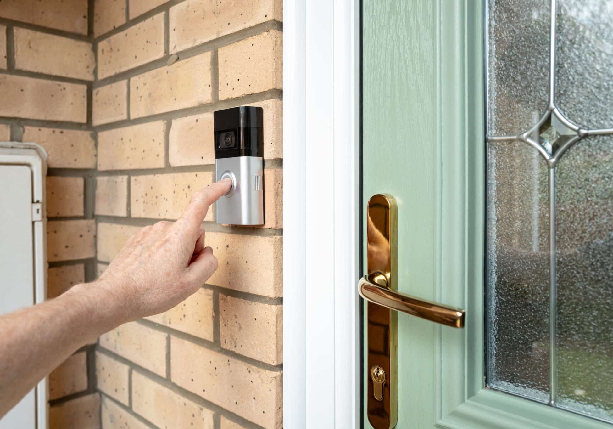 Visitor seen pressing the door bell button of a wireless smart home door bell which has an integrated camera and two-way audio. The door is a new, high security uPVC door.