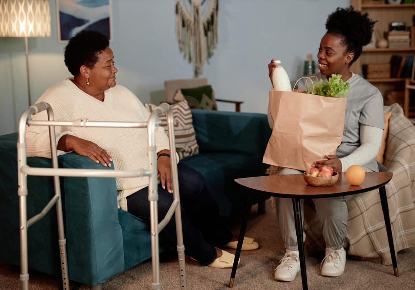 Black Female Social Worker Helping Senior Woman With Disability Delivering Groceries At Home Community Health Worker helps a woman who had a recent fall gain access to healthy food at home